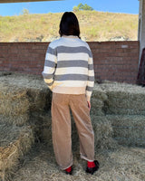MAGLIONE A RIGHE ANTRACITE E PANNA indossato da donna in un ambiente rustico con fieno sullo sfondo.