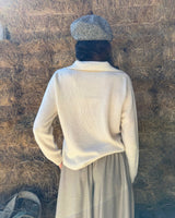 Maglione cashmere scollo a polo cremoso, indossato con gonna, vista posteriore su sfondo naturale di paglia.
