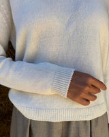 Maglione cashmere scollo a polo crema con maniche lunghe e dettagli a costine, indossato da una persona.