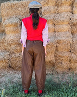 PANTALONE BAGGY IN ECOLEATHER BROWN worn by a model with a red vest against a backdrop of hay bales.