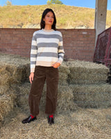 PANTALONE BAGGY IN VELLUTO CASTAGNO worn with a striped sweater, set against a backdrop of hay bales.