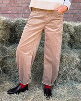 PANTALONE BAGGY IN VELLUTO COGNAC displayed on model against hay backdrop, showcasing its relaxed fit and soft texture.