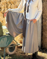 GONNA PANTALONE IN FLANELLA SABBIA indossata con maglione e cravatta in uno scenario campestre.