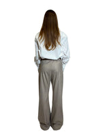 Modella di spalle che indossa pantalone sabbia lievemente gessato con camicia bianca.