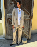 PANTALONE SABBIA LIEVEMENTE GESSATO indossato con giacca e camicia in un ambiente rustico.