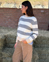 MAGLIONE A RIGHE ANTRACITE E PANNA indossato da modella in un ambiente rustico.