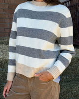 MAGLIONE A RIGHE ANTRACITE E PANNA indossato con pantaloni in velluto, su sfondo di paglia.