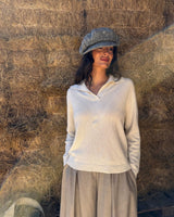 Maglione cashmere scollo a polo in crema indossato da donna con cappello grigio, sullo sfondo di fieno.