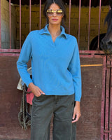 MAGLIONE CON SCOLLO A POLO CELESTE indossato da una donna con occhiali da sole in una stalla.