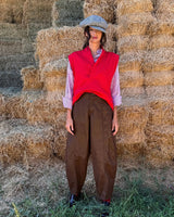 Model wearing PANTALONE BAGGY IN ECOLEATHER BROWN with a red top and hat, standing in front of hay bales.
