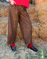 PANTALONE BAGGY IN ECOLEATHER BROWN displayed outdoors against a rustic hay background, showcasing its contemporary design.