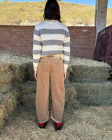 PANTALONE BAGGY IN VELLUTO COGNAC worn with a striped sweater, viewed from the back, standing on hay bales.