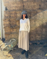 Modella che indossa la GONNA PANTALONE IN FLANELLA SABBIA davanti a un muro di paglia.