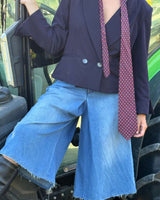 Modella che indossa una giacca crop doppiopetto sofisticata con cravatta e pantaloni di jeans chiari.