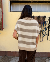 Gilet oversize righe cashmere beige e panna visto da dietro, con scollo a V e spalla scesa in un contesto rustico.
